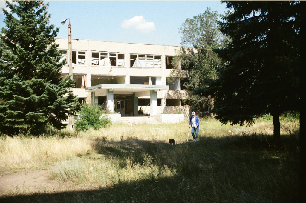 A man walks his dog in front of a school destroyed by a Russian guided aerial bomb. Kramatorsk, August 2026. Yulia Kalaban for JAMnews.